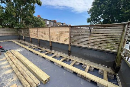 Close-up view of a Wimbledon roof terrace showing new perimeter cladding, privacy fencing, and decorative plant pots.