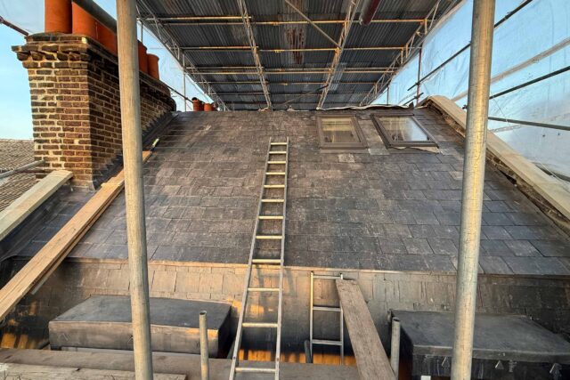 Natural slate roof tiles under temporary scaffolding during a slate roof replacement in London.
