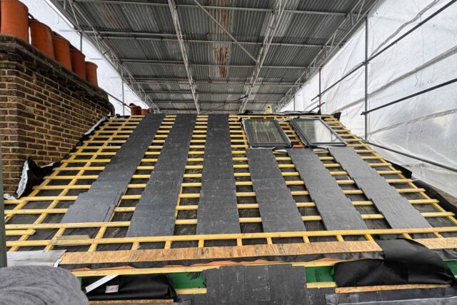 Timber battens and stacked slates under scaffolding during a slate roof replacement in London.