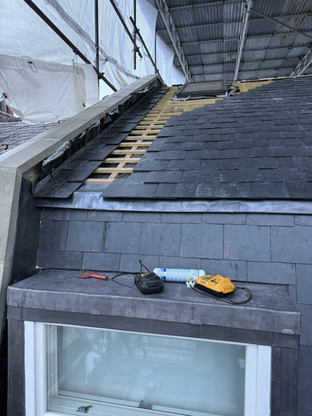 Slate tiles being laid onto timber battens during a slate roof replacement in London.